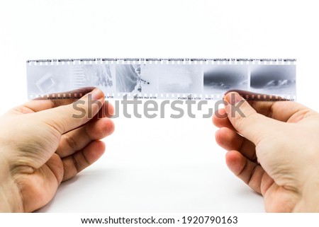 hands holding 35mm photographic film negatives on white background