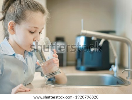 Young caucasian girl is holding a glass with water. Concept of good quality clean water. Kitchen faucet. Pouring fresh drink. Hydration. Healthy lifestyle. World water day. Environmental problem Royalty-Free Stock Photo #1920796820