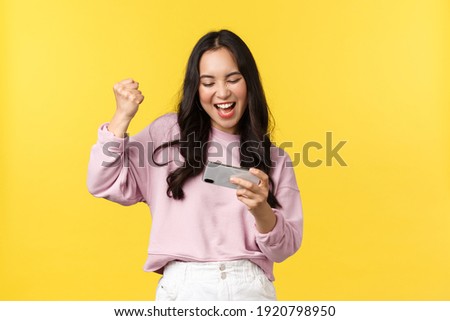 People emotions, lifestyle leisure and beauty concept. Enthusiastic asian girl gamer playing on mobile phone, tilting smartphone to pass level in game, smiling amused, fist pump as winning Royalty-Free Stock Photo #1920798950