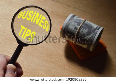 Top view of money banknote and magnifying glass written with text BUSINESS TIPS.