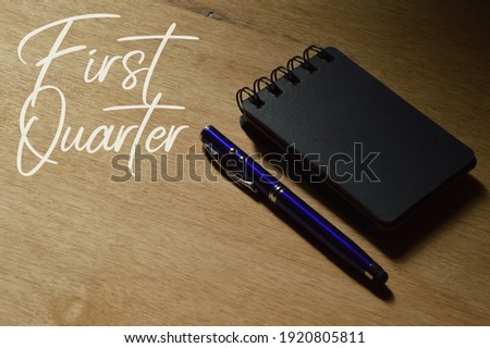 Top angle view of pen and notebook over wooden background written with FIRST QUARTER.