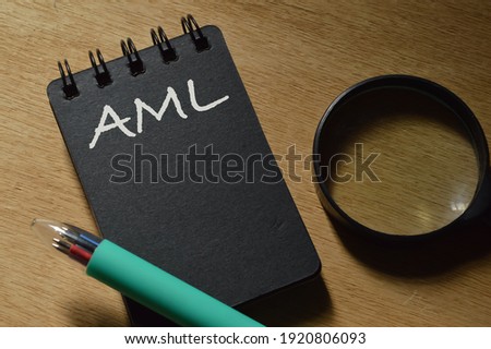 Tip view of pen, magnifying glass and notebook written with AML stands for Anti Money Laundering