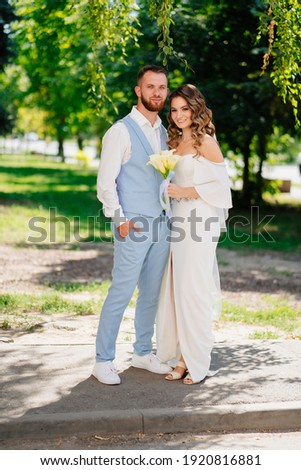 beautiful and happy newlyweds in the summer park. Groom in a blue suit and bride in an elegant white dress with a bouquet of calla flowers. Wedding fashion.