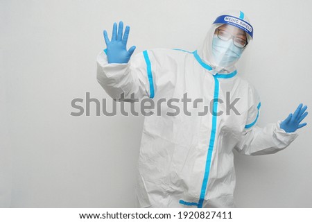 Frontliner in happy mood do silly dancing in white and blue stripe jumpsuit wearing transparent protective shield handling Covid-19 situation with clean white background and copyspace.