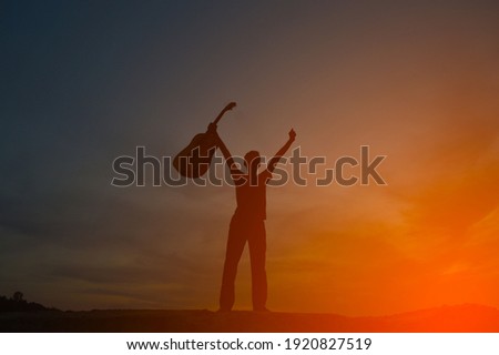 The shadow of a man holding a guitar on a hill with orange light