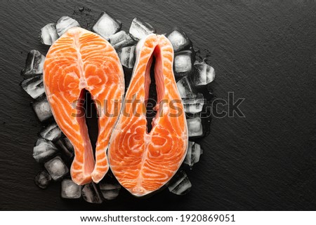 chilled salmon steak in lettuce and ice on a stone background, top view, place for text