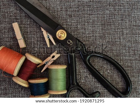 sewing tools. black scissors, spools of thread on baggy fabric. horizontal photo. Needlework tool. retro sewing tools: old scissors, bobbins of thread on gray fabric. Tailor.