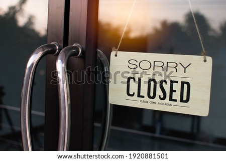 The board hung in front of the glass door of the coffee shop had a  message sorry and closed. Light from the soft sun in the morning was bright as the background. Reflection from nature, sky, trees
