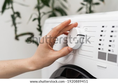 Selective focus on settings button at modern automatic washing machine. Close up view of cropped woman hand turning knob and choosing program for daily laundry at home Royalty-Free Stock Photo #1920889451
