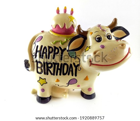 Smiling Cow Figurine with Black Happy Birthday Text and Birthday Cake with Candles. Mascot Celebrating Birthdays Isolated in White Background.