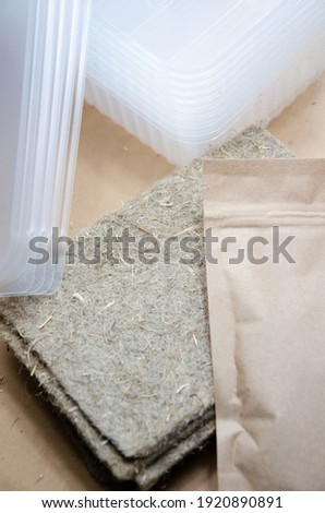 Closeup linen growing mat and packaging with microgreen seeds. Kit for growing microgreens at home: linen substrate, seeds in package and plastic bowls with lids. Selective focus. Home garden concept.