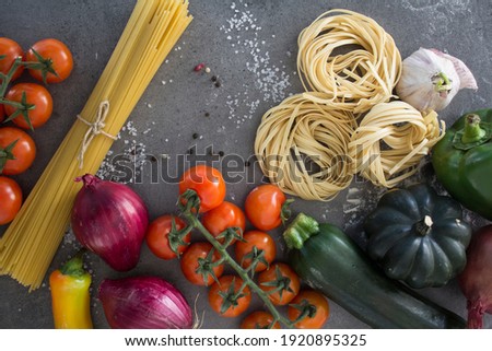 Top view photo of fresh organic vegetables, raw tagliatelle pasta on gray textured background with copy space. Healthy eating concept. Traditional Italian food receipts. 