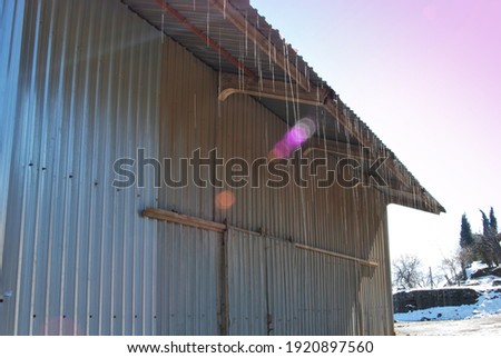 metal building and the bright sky. From the roof dripping drops of water, precipitation, thawing of snow. Silhouette of a dark roof against the sky.