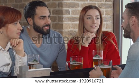 Group of friends talking over glass of beer at the pub. Young people enjoying drinking beer together at the bar, talking joyfully. Communication, friendship concept
