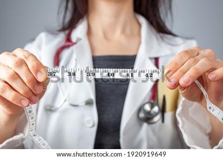 Close up isolated image of a caucasian doctor holding a tape measure in her hands which shows 40 inches as abdominal circumference upper limit in healthy people. Concept for weigh loss and fitness. Royalty-Free Stock Photo #1920919649