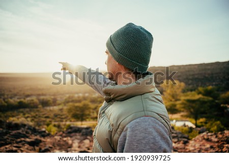 Caucasian male free spirit pointing at sunset in distance while walking in wilderness