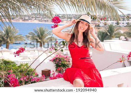 Caucasian happy tourist woman is sitting at the terrace with view on the sea. Resting girl is smiling. Relaxing beautiful female on travel vacation. Summer concept. Outdoor (Sharm El Sheikh, Egypt). 