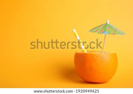 Orange with straw and small paper umbrella as summer cocktail on yellow background. Space for text