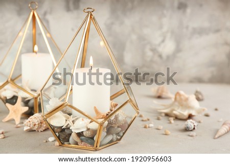 Stylish glass holders with burning candles, seashells and pebbles on light stone table Royalty-Free Stock Photo #1920956603