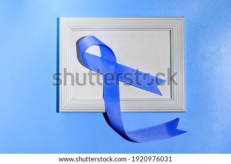 Blue ribbon with white frame on blue background with copy space. Colorectal Cancer Awareness. Colon cancer of older person. World diabetes day.