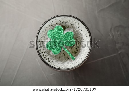 Glass of beer with clover leaf on grey table, top view. St Patrick's Day celebration