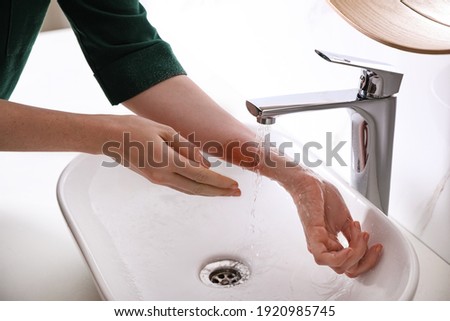 Woman putting burned hand under running cold water indoors, closeup Royalty-Free Stock Photo #1920985745