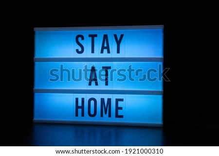 blue illuminated sign with stay at home written on it.