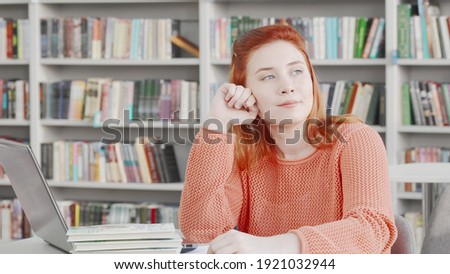 Young female student looking away thoughtfully studying at college library