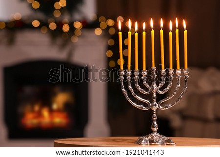 Silver menorah in room with fireplace, space for text. Hanukkah symbol
