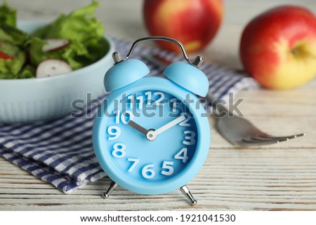 Alarm clock and healthy food on white wooden table, closeup. Meal timing concept