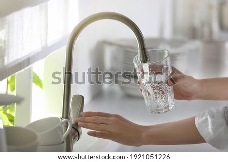Woman pouring water into glass in kitchen, closeup Royalty-Free Stock Photo #1921051226