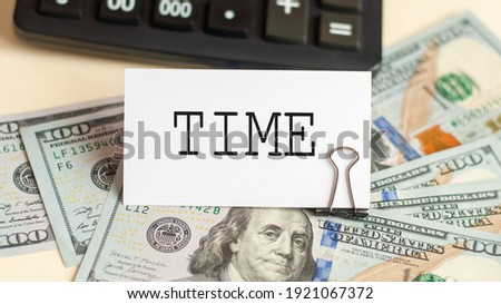 The word time is written on the white card. Card on the background of 100 dollar bills and a calculator. Business concept