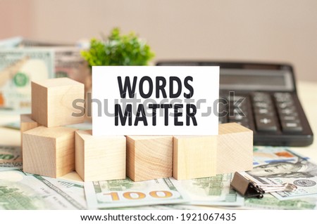 White paper card with text WORDS MATTER on the wooden blocks. Banknotes, black calculator and green plant in the background. Business concept. Brown background.