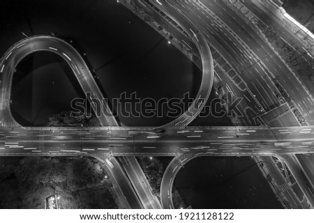 drone top down shot of road system with freeway interchange, traffic, bridge, ramps and loops at night over a river in Black and white.