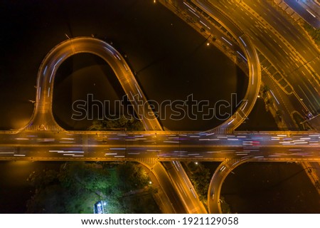 colorful drone top down shot of road system with freeway interchange, traffic, bridge, ramps and loops at night over a river
