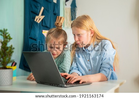 Children receive education at home in a classroom with a laptop, online courses for children, child development, two caucasian girls have fun and watch cartoons, homeshooling 
