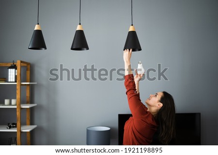 Woman Changing Broken Light Bulb To LED Royalty-Free Stock Photo #1921198895