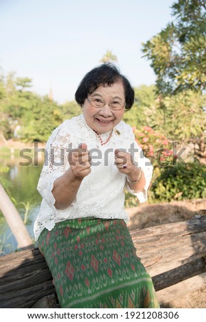 This image of a beautiful Asian old woman from Thailand wearing a traditional clothing stands smiling happily doing boxing poses.