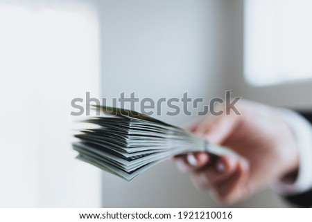 One hundred dollar bills money bundle, in hand of man in suit and white shirt. Blurred background. High quality photo