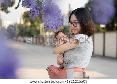 asian woman mother wearing support belt holding baby infant with flower at neighborhood. local place near home.