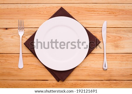 White plate, knife and fork on wooden table with tablecloth and copyspace 