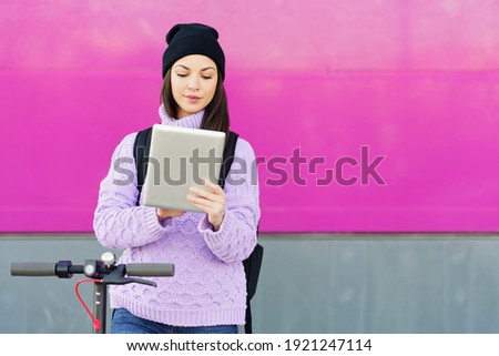 Woman in her twenties with electric scooter using digital tablet outdoors. Lifestyle concept.