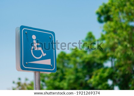 Wheelchair ramp sign mounted on pillar, with tree and sky background.