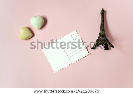 Blank postcard and decorative elements (two stone hearts and a souvenir Eiffel tower) on pink background, empty postcards, postcrossing, mockup. Top view, flat lay. Selective focus. Copy space.