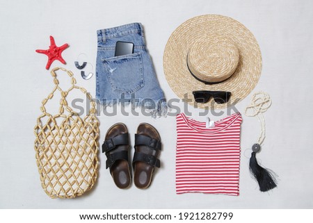 Simple summer outfit, denim shorts and striped cotton shirt with accessories on white background. Women's casual fashion items, top view.