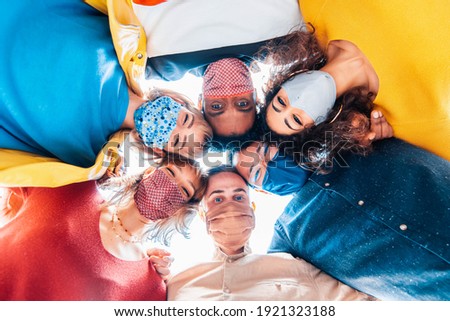 Multiracial group of friends wearing protective face masks taking a selfie - New normal friendship concept with young people looking down at camera and laughing - Bright filter Royalty-Free Stock Photo #1921323188