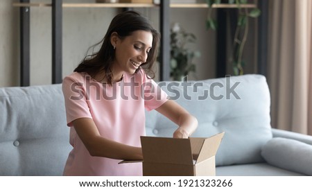 Hopeful excited young mixed race female prepare moving relocation to new house pack things to cardboard box. Curious arabian woman customer of internet store receive unpack parcel with consumer goods Royalty-Free Stock Photo #1921323266