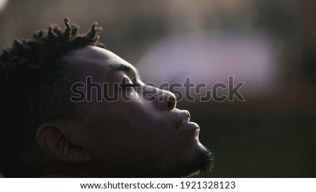 Hopeful African man looking up at sky, black person closing eyes in meditation and contemplation