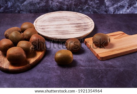 Several kiwis on wooden elements. Wooden plate, and several wooden boards, dark stone floor and dark marble background.