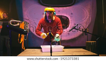 Man in face shield breaking glass while male colleague clinking metal chains against screen with 3D cartoon about robot